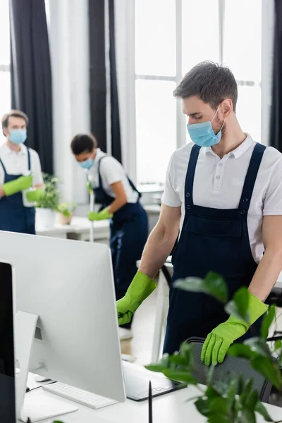 Cleaner em máscara médica de pé perto do computador e tablet gráfico no escritório — Fotografia de Stock