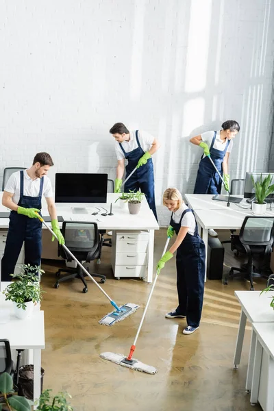 Limpiadores multiétnicos lavando piso en oficina moderna - foto de stock