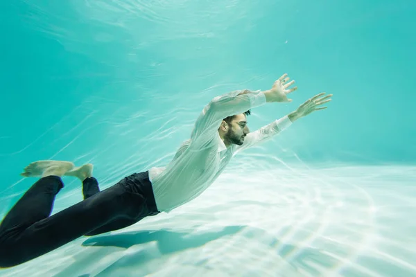 Мусульманский мужчина в формальной одежде плавает над дном в бассейне — стоковое фото