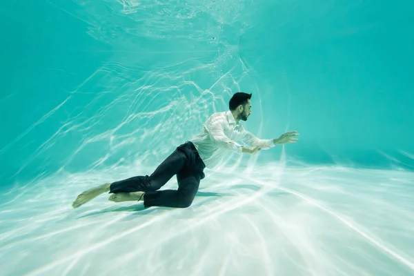 Homem de negócios árabe nadando perto do fundo com ondulação na piscina — Fotografia de Stock
