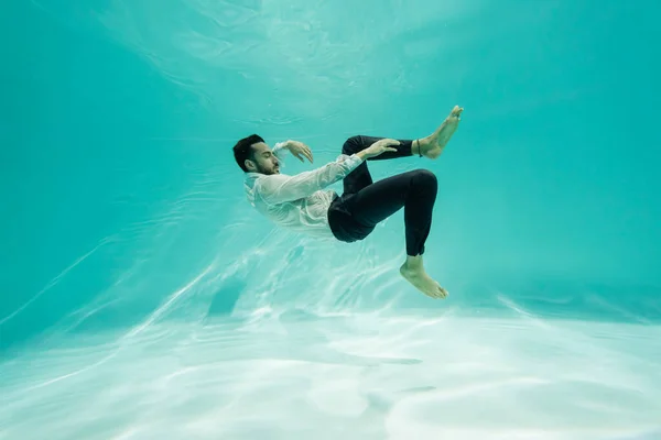 Hombre de negocios árabe en pantalones y camisa nadando bajo el agua en la piscina - foto de stock