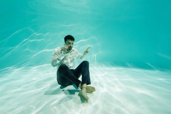 Арабский бизнесмен разговаривает по смартфону и показывает пальцем под водой — стоковое фото