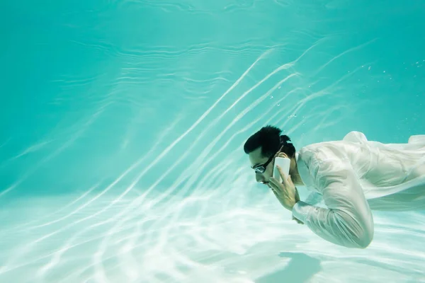 Uomo d'affari musulmano in maschera che parla sul cellulare sott'acqua in piscina — Foto stock