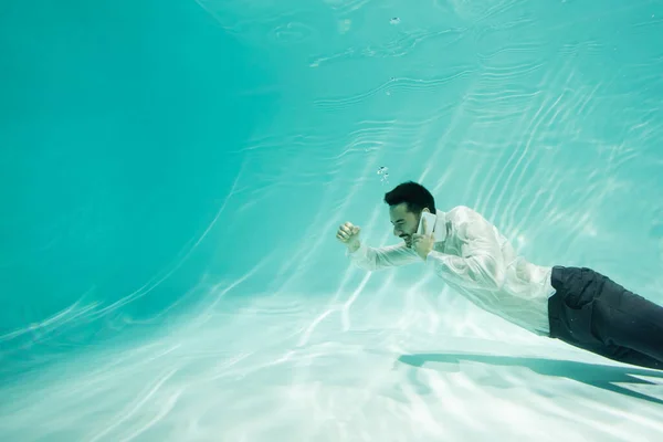 Homme d'affaires arabe joyeux parlant sur téléphone portable et montrant un geste oui dans la piscine — Photo de stock