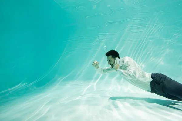 Alegre hombre de negocios árabe hablando por celular y mostrando sí gesto en la piscina - foto de stock