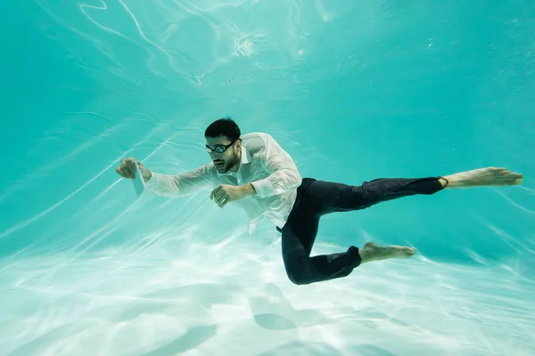 Uomo d'affari musulmano in maschera che tiene il telefono cellulare sott'acqua in piscina — Foto stock