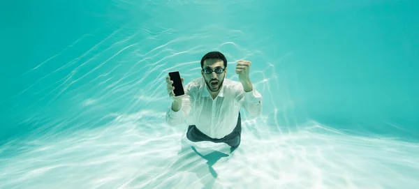 Возбужденный мусульманский бизнесмен в очках показывает да жест и смартфон в бассейне, баннер — стоковое фото