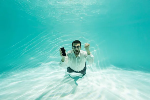 Homme d'affaires musulman en lunettes tenant un smartphone et montrant un geste oui sous l'eau — Photo de stock