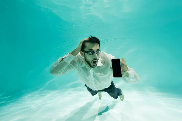 Здивований аравійський бізнесмен тримає смартфон з чистим екраном під водою. — стокове фото