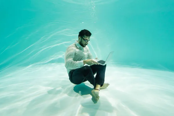 Hombre de negocios árabe usando el ordenador portátil bajo el agua en la piscina - foto de stock