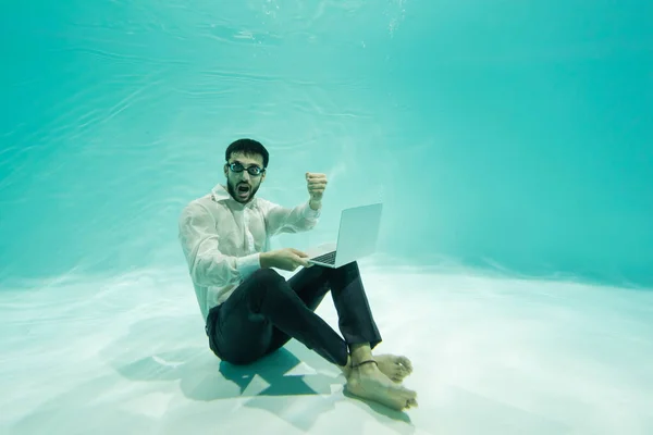 Emocionado hombre de negocios musulmán mostrando sí gesto y la celebración de la computadora portátil en la piscina - foto de stock