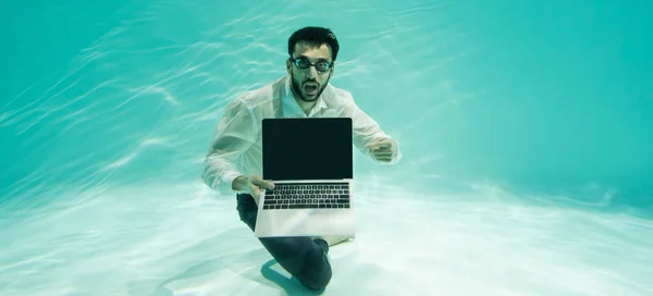 Мусульманский бизнесмен в очках указывает на ноутбук с чистым экраном в бассейне, баннер — стоковое фото