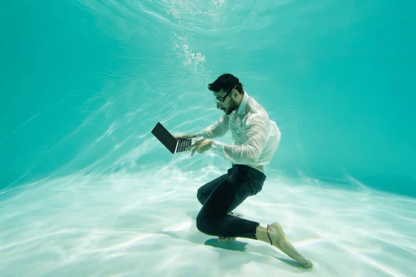 Muslim manager in formal wear and goggles using laptop underwater — Stock Photo