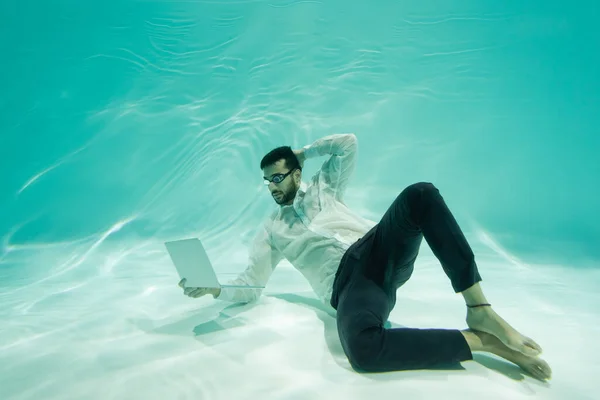 Hombre de negocios árabe mirando a la computadora portátil mientras nada bajo el agua - foto de stock