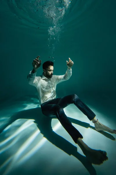 Hombre árabe en ropa formal nadando cerca de burbujas de aire en la piscina - foto de stock