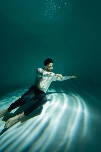 Muslim businessman swimming near bottom of pool with light — Stock Photo