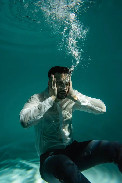 Арабский бизнесмен с руками возле головы плавает под водой в бассейне — стоковое фото