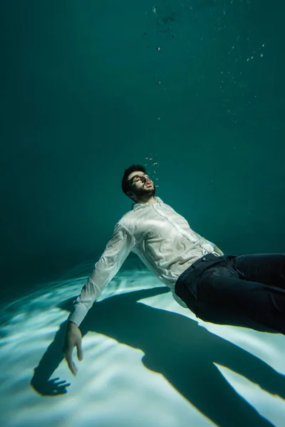 Hombre musulmán en ropa formal flotando cerca de burbujas de aire en la piscina - foto de stock