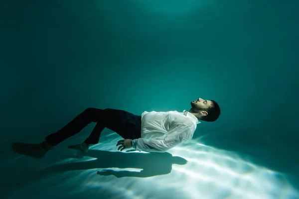 Joven hombre de negocios árabe barbudo nadando en luz bajo el agua - foto de stock