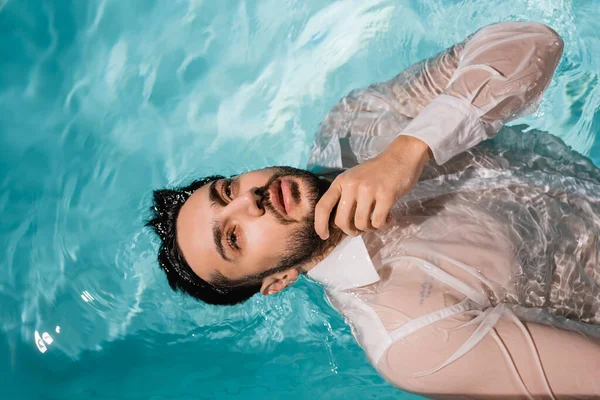 Top view of bearded arabian businessman in shirt swimming in pool — Stock Photo