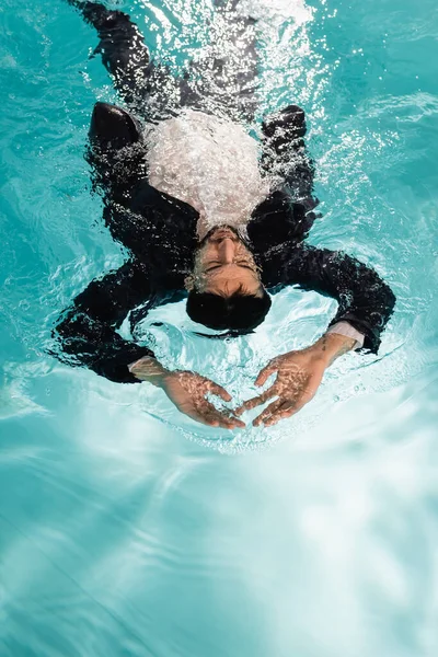 Высокий угол обзора мусульманского бизнесмена в костюме плавающего в бассейне — стоковое фото