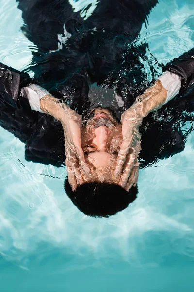 Vista superior del hombre musulmán en traje tocando la cara bajo el agua en la piscina - foto de stock