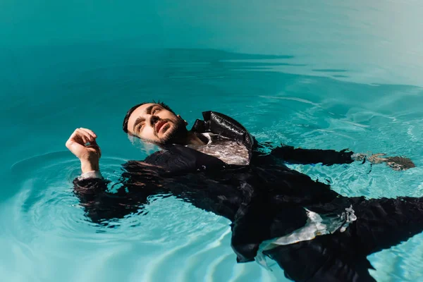 Hombre de negocios árabe en ropa formal mirando hacia otro lado mientras nada en la piscina - foto de stock