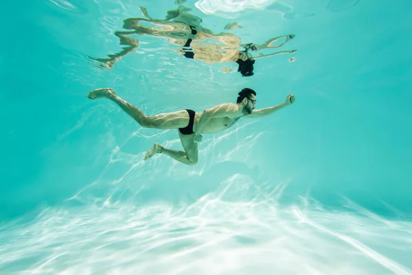 Maillot de bain arabe en lunettes plongeant en piscine avec de l'eau turquoise — Photo de stock