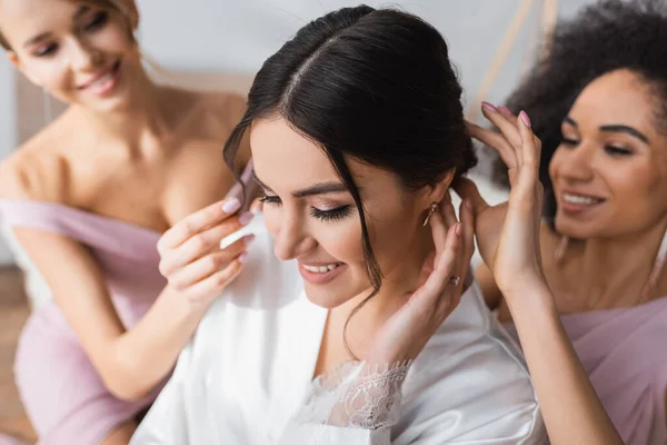 Madrinhas inter-raciais fazendo penteado para noiva feliz, fundo borrado — Fotografia de Stock