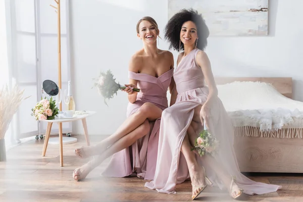 Encantadoras damas de honra multiculturais sentadas na cama com buquês de casamento — Fotografia de Stock