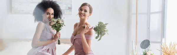 Femmes multiculturelles gaies tenant des bouquets de mariage dans la chambre, bannière — Photo de stock