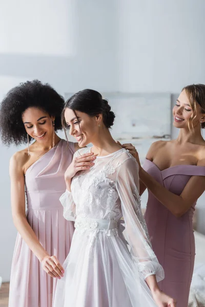 Damas de honor interracial preparando mujer feliz para la boda - foto de stock