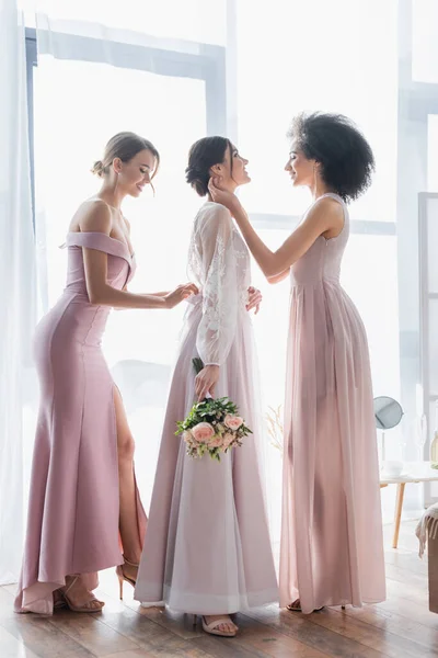 Side view of interracial bridesmaids preparing bride for wedding — Stock Photo