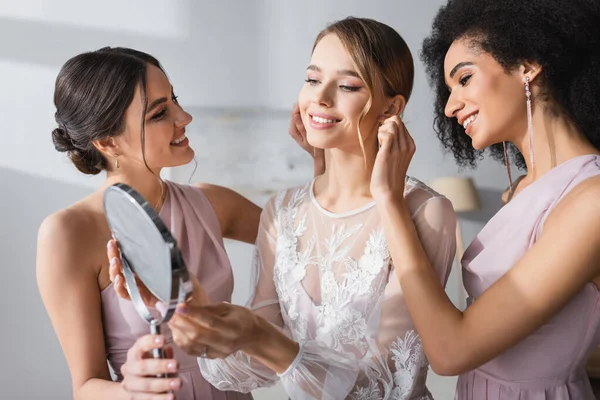 Jeune mariée regardant dans le miroir près des amis interraciaux la préparer pour le mariage — Photo de stock