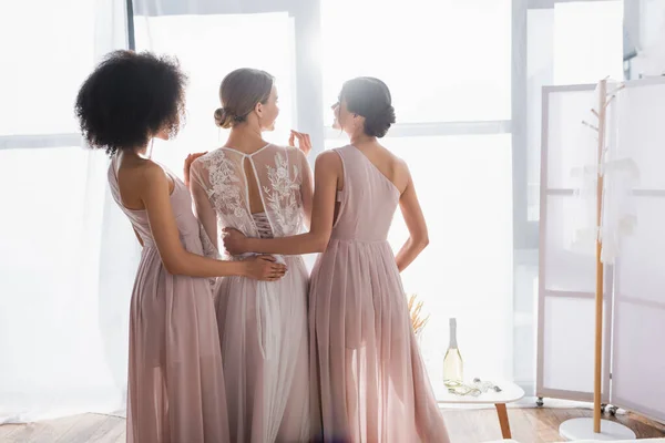 Demoiselles d'honneur élégantes embrassant jeune mariée le matin ensoleillé à la maison — Photo de stock