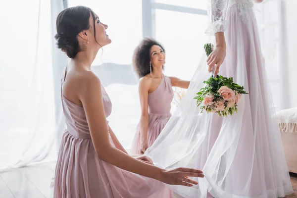 Felice damigelle multiculturali guardando sposa tenendo bouquet di nozze — Foto stock