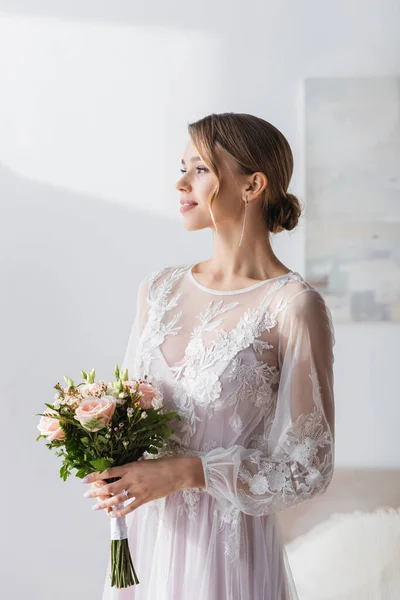 Giovane sposa in abito da sposa bianco tenendo bouquet e guardando lontano a casa — Foto stock