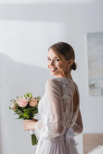 Mariée heureuse avec bouquet de mariage souriant à la caméra à la maison — Photo de stock