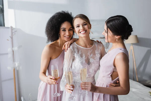 Freudige Braut blickt in die Kamera und hält Champagner mit interrassischen Freunden zusammen — Stockfoto