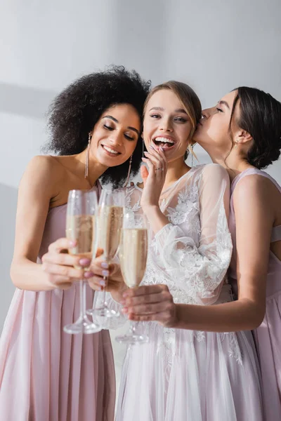 Mariée excitée regardant la caméra tout en cliquetis verres à champagne avec des amis multiculturels — Photo de stock