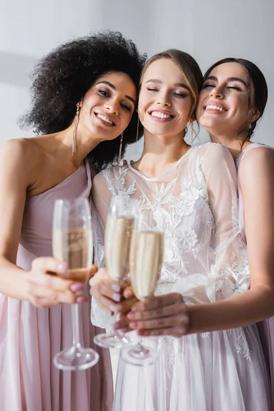 Fröhliche Braut mit Brautjungfern, die Champagnergläser auf verschwommenem Vordergrund klirren — Stockfoto