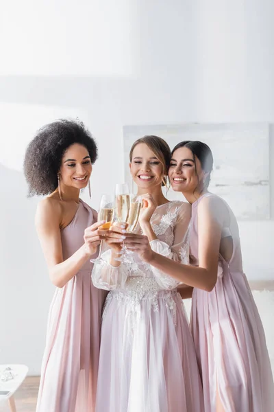 Alegres damas de honor interracial tintineo copas de champán con novia en el dormitorio - foto de stock