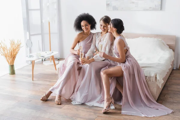 Elegante Braut mit multikulturellen Brautjungfern mit Champagnergläsern im Schlafzimmer — Stockfoto