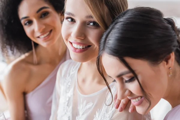 Selektiver Fokus einer jungen Braut, die in der Nähe interrassischer Brautjungfern in die Kamera lächelt — Stockfoto