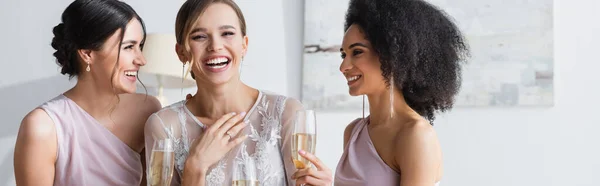Взволнованная невеста смеется рядом с друзьями, держа бокалы шампанского, баннер — стоковое фото