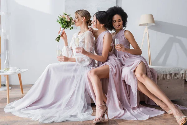 Young bride enjoying flavor of wedding bouquet near interracial bridesmaids — Stock Photo