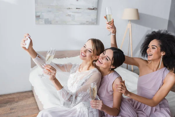 Возбужденная невеста делает селфи с межрасовыми друзьями в спальне — стоковое фото