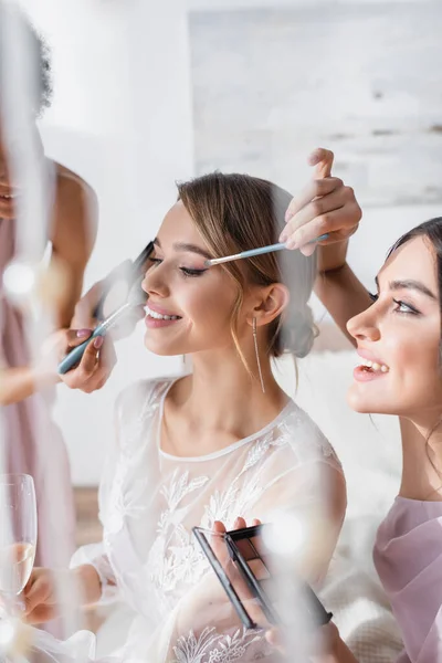 Multicultural bridesmaids doing visage to happy bride on blurred foreground — Stock Photo