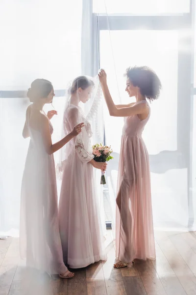 Vue latérale de la femme afro-américaine levant voile de jeune mariée à la maison — Photo de stock