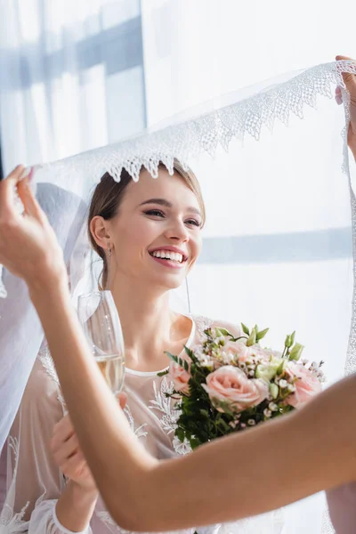 Demoiselle d'honneur tenant voile de mariée joyeuse avec bouquet de mariage et champagne — Photo de stock